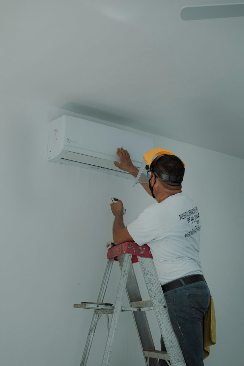 Person installing an air conditioning unit on a white wall.